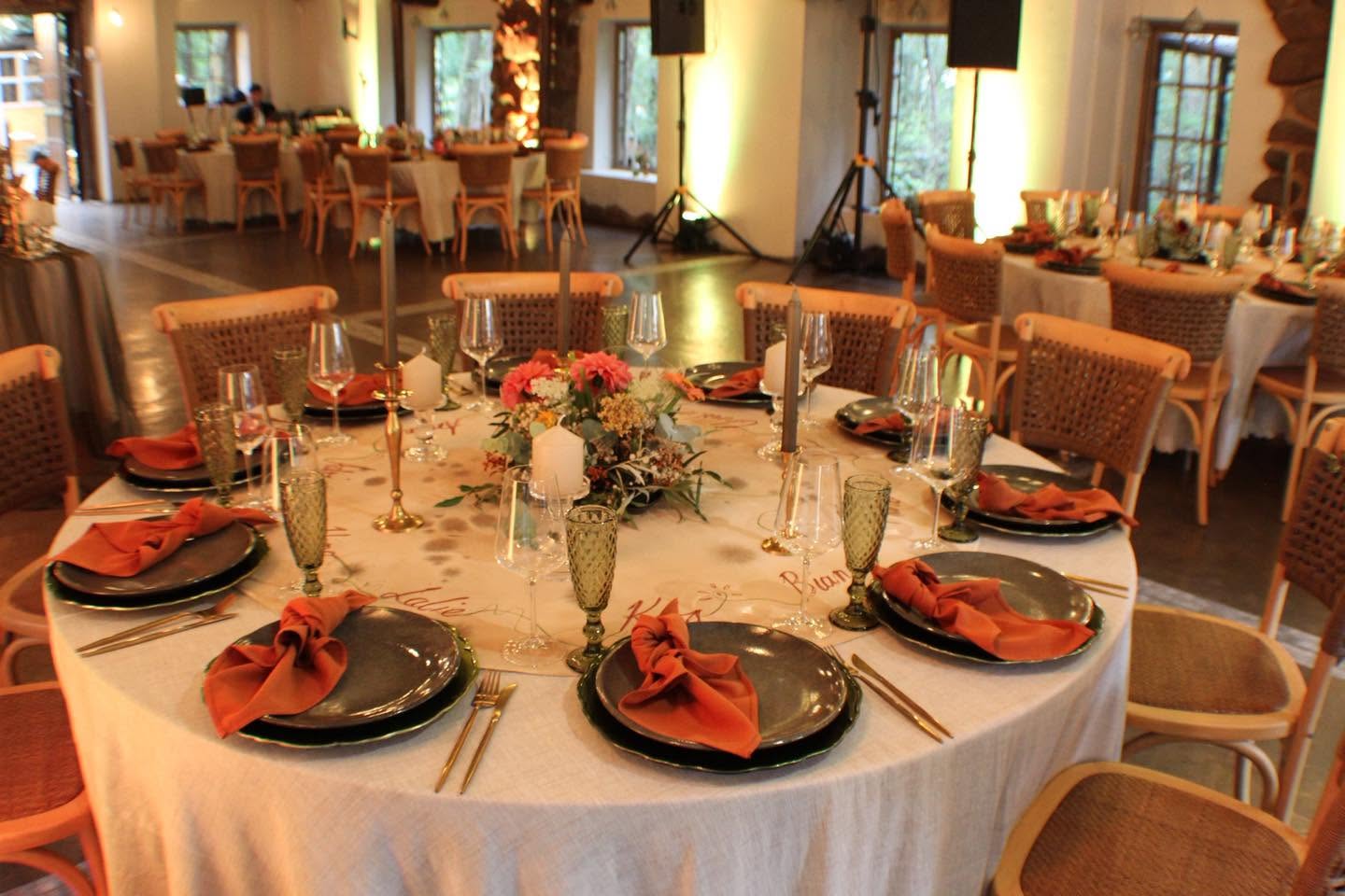 Round tables at Kleinbosch set with woven chairs, flowers, candles and warm terracotta napkins